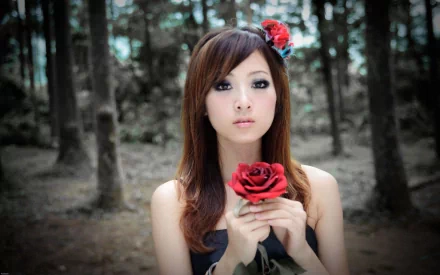 HD desktop wallpaper featuring a woman holding a red rose in a forest, with a red flower in her hair, exuding a serene and enchanting ambiance.
