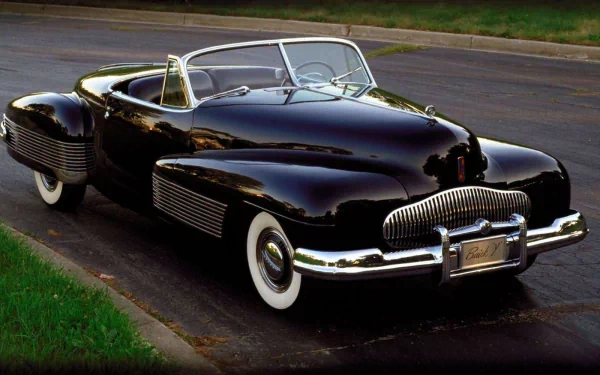 HD PC desktop wallpaper: glossy black 1940s Buick Y-Job convertible parked on a street, whitewall tires and chrome grille reflecting light.