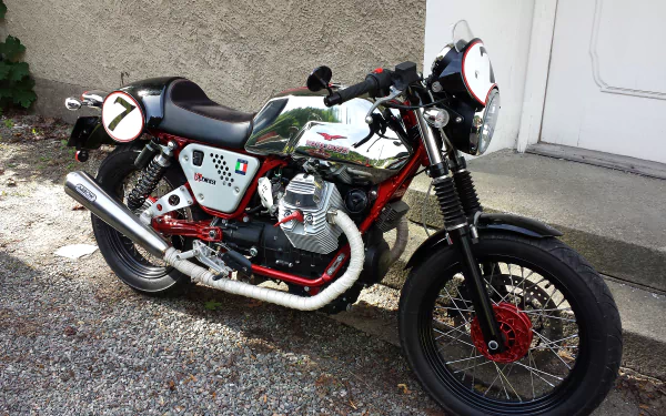 HD desktop wallpaper featuring a classic Moto Guzzi motorcycle parked on a gravel surface near a building wall.