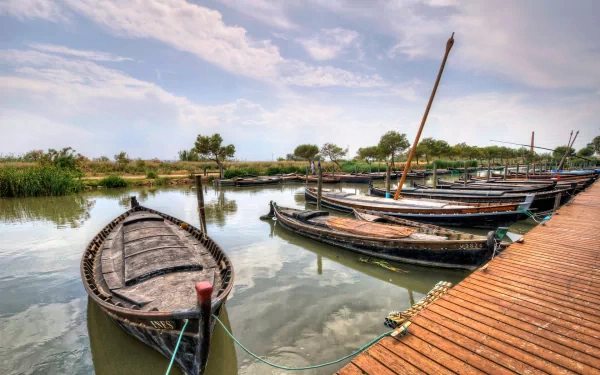 HD PC desktop wallpaper featuring several wooden boats moored along a calm waterfront with a partly cloudy sky and lush greenery in the background.
