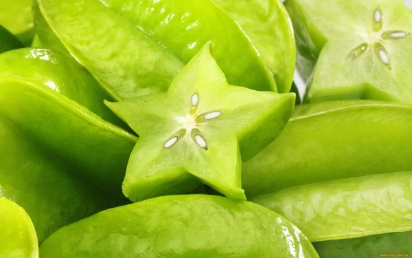 Vibrant starfruit, showcasing its unique star shape, sits among glossy green leaves, creating a fresh and appetizing visual for an HD desktop wallpaper.
