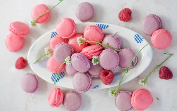 HD desktop wallpaper featuring a plate of pink and purple macarons with raspberries and delicate flowers on a light background.