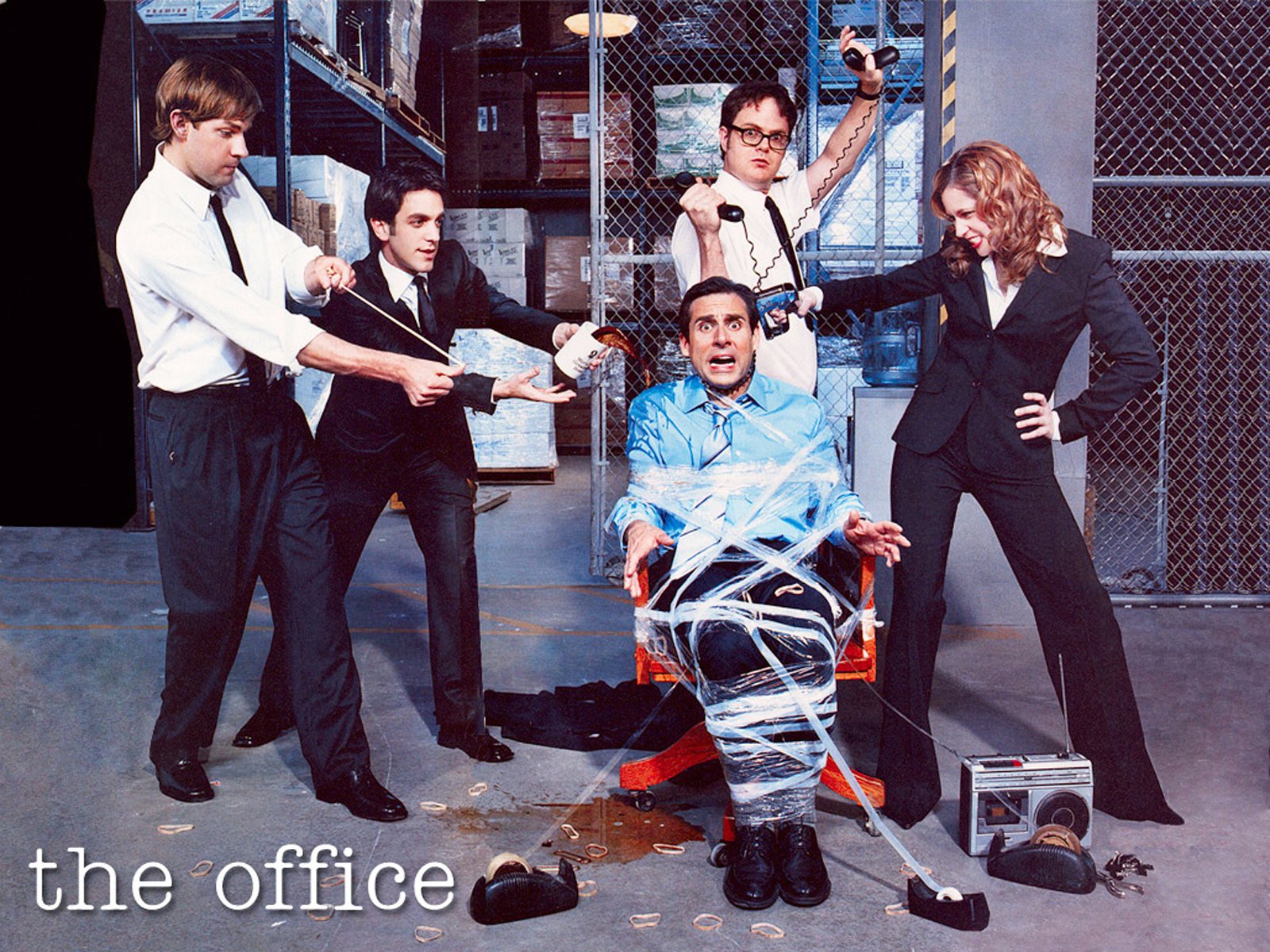 A vibrant HD wallpaper featuring characters from the US TV show The Office, with a comedic scene of Michael Scott tied up and surrounded by coworkers in a playful office setting.