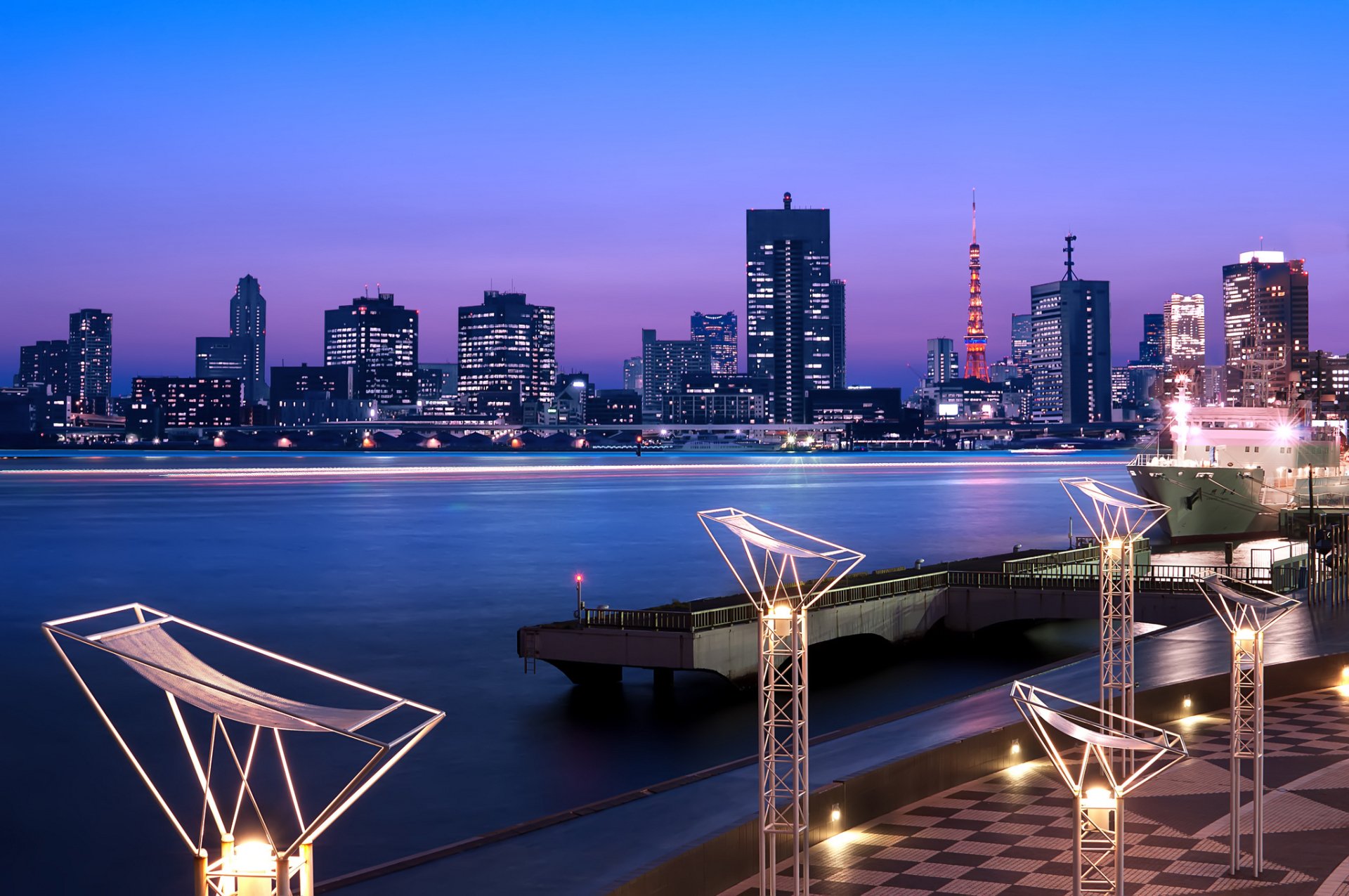 HD desktop wallpaper showing a man-made Tokyo cityscape at dusk with illuminated buildings and a calm waterfront under a purple-blue sky.