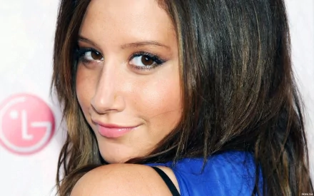 HD desktop wallpaper featuring a close-up of celebrity Ashley Tisdale with a soft smile and long, dark hair against a light background.