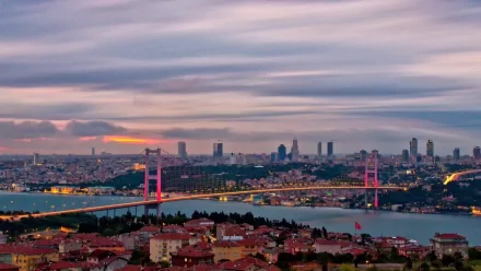 HD wallpaper featuring a panoramic view of Istanbul, Turkey, showcasing the Bosphorus Bridge illuminated amidst the cityscape at dusk.