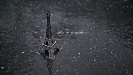 HD desktop wallpaper featuring a miniature Eiffel Tower on a textured surface with the phrase How can saying do... subtly visible in the background.
