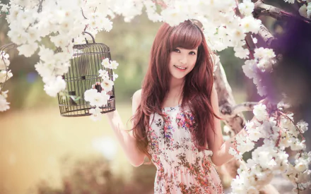 HD desktop wallpaper featuring an Asian woman smiling, holding a birdcage, surrounded by blooming white flowers.