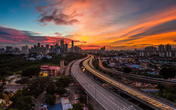 A stunning Kuala Lumpur skyline at sunset, highlighting the city's modern architecture and vibrant colors, with a winding highway leading into the heart of Malaysia.