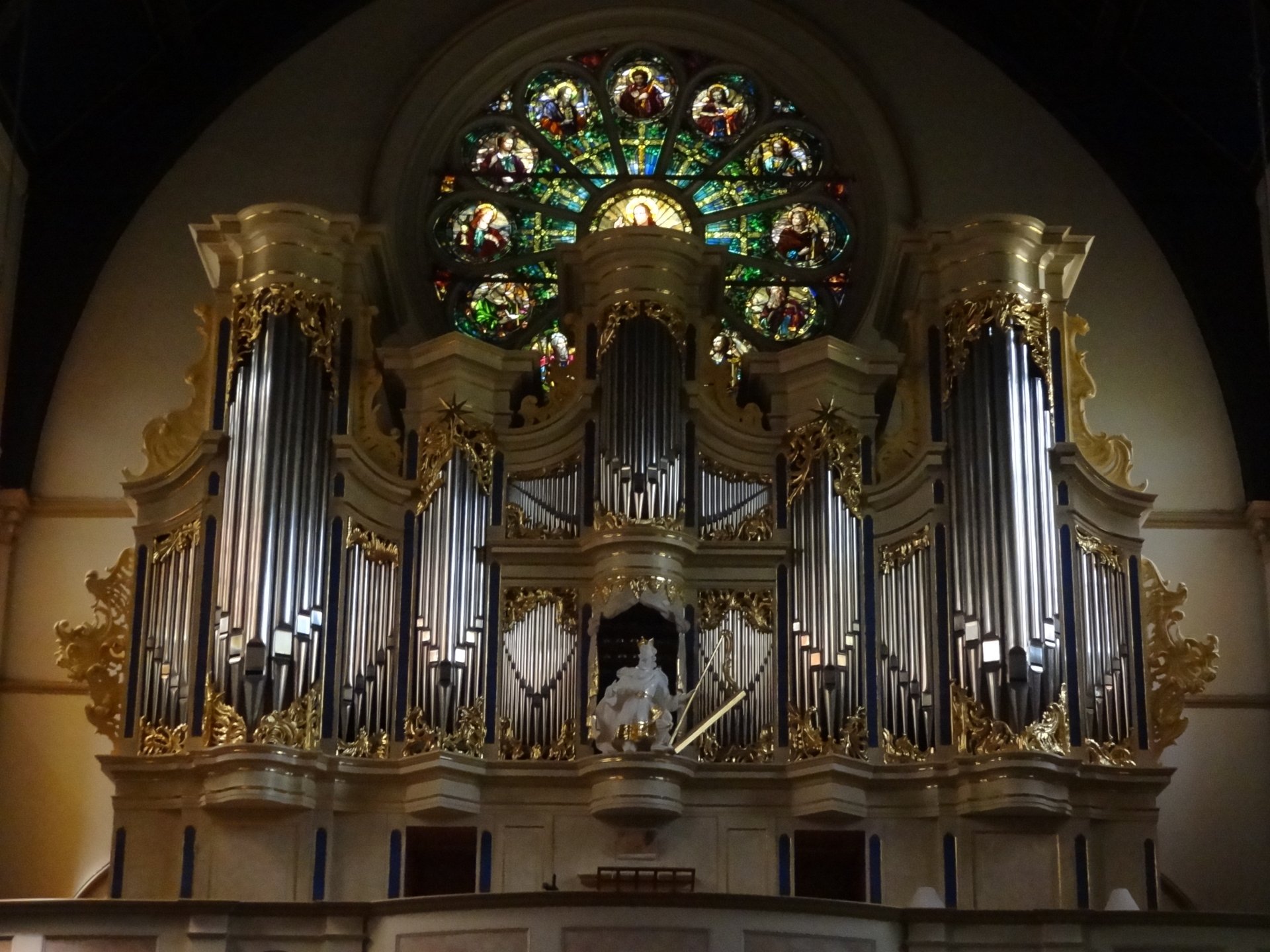 4K Ultra HD image of a grand church pipe organ with ornate gold details beneath a vibrant stained glass rose window, capturing religious architecture and artistry.
