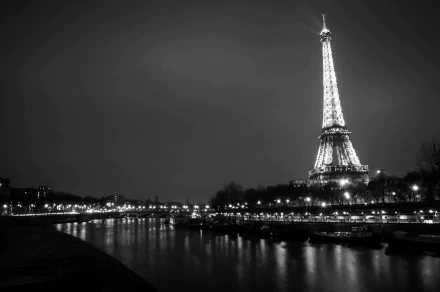 Black and white 4K Ultra HD night view of the illuminated Eiffel Tower reflecting on the river in Paris, France, showcasing iconic man-made architecture and city lights.