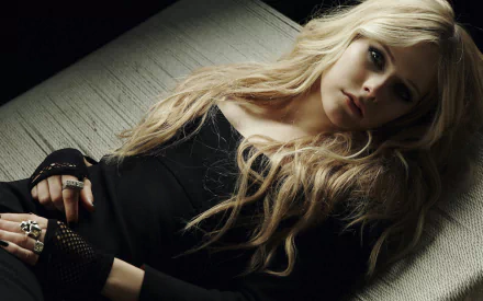 HD desktop wallpaper featuring Avril Lavigne lying down, with long blonde hair and a black outfit, capturing a moody music-themed portrait.