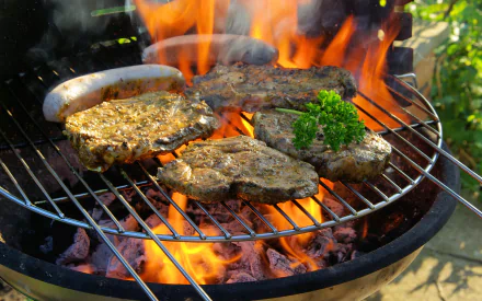 A vibrant barbecue scene featuring sizzling steaks and sausage on a grill, surrounded by flames and garnished with parsley, captured in high-definition for a desktop wallpaper.