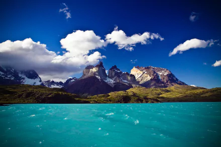 HD desktop wallpaper showcasing the vibrant blue lake and striking mountain peaks of Torres del Paine under a bright sky with scattered clouds.