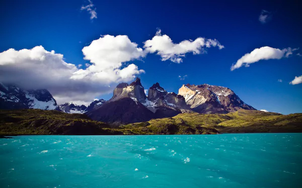 HD desktop wallpaper showcasing the vibrant blue lake and striking mountain peaks of Torres del Paine under a bright sky with scattered clouds.