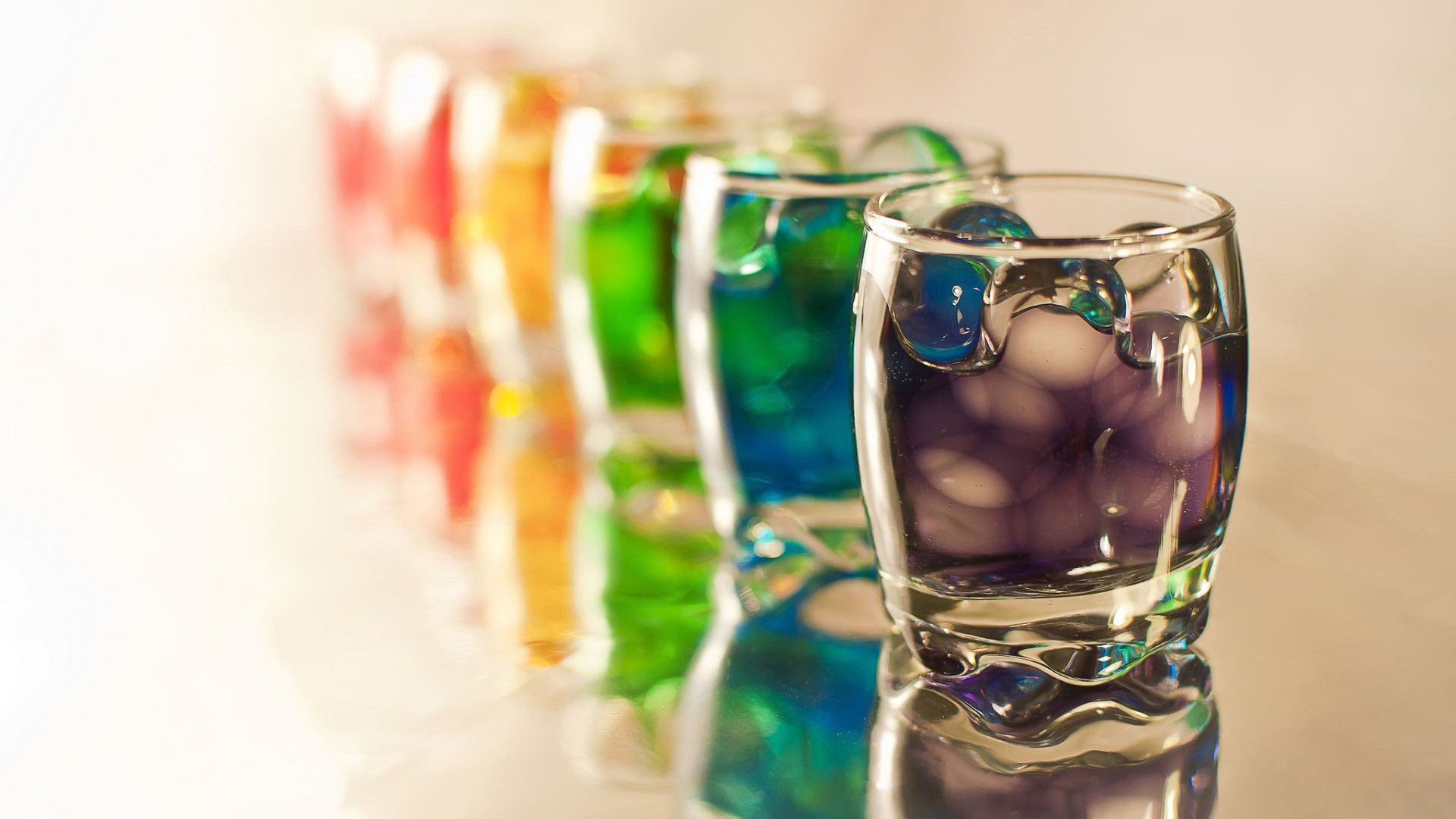 A vibrant arrangement of glasses with colorful liquids, beautifully reflecting light, creates a captivating HD desktop wallpaper backdrop bursting with color.