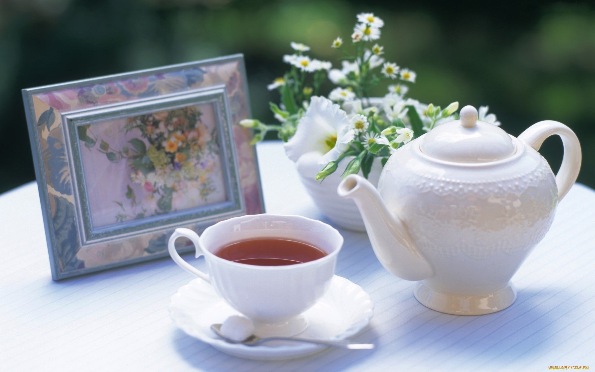 HD PC desktop wallpaper featuring a white teapot, a cup of tea with a sugar cube, a small bouquet of white flowers, and a framed floral painting on a white table.