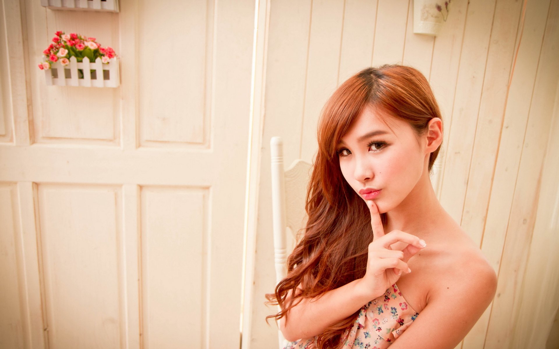 HD desktop wallpaper of an Asian woman with long brown hair, posing against a beige wooden wall with small flower pots.