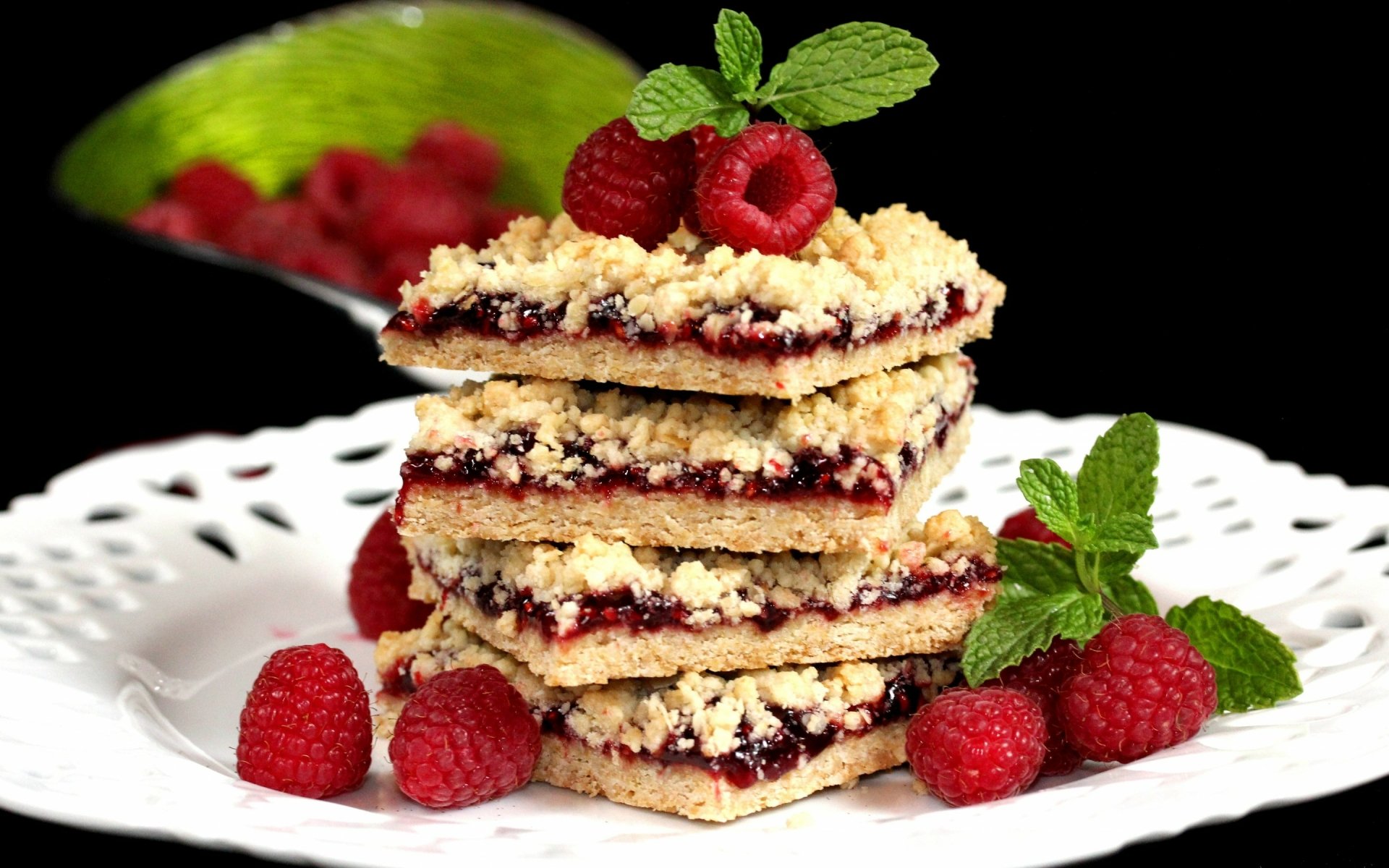 HD desktop wallpaper showing a stack of crumb-topped berry pies garnished with fresh raspberries and mint on a white plate against a black background.