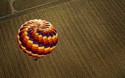 A vibrant hot air balloon floats over a patchwork of fields, creating a striking contrast against the earthy tones of the landscape. Ideal HD wallpaper for desktop backgrounds.