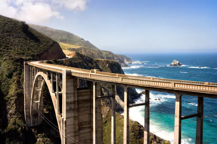 HD wallpaper of a scenic bridge spanning a rugged coastline with clear blue seas, set against green hills under a bright sky.