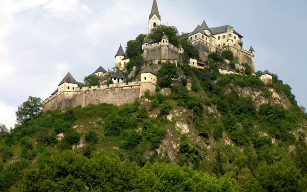 A stunning HD wallpaper of Hochosterwitz Castle perched atop a hill, surrounded by lush greenery and a dramatic sky, showcasing an impressive example of man-made architecture.