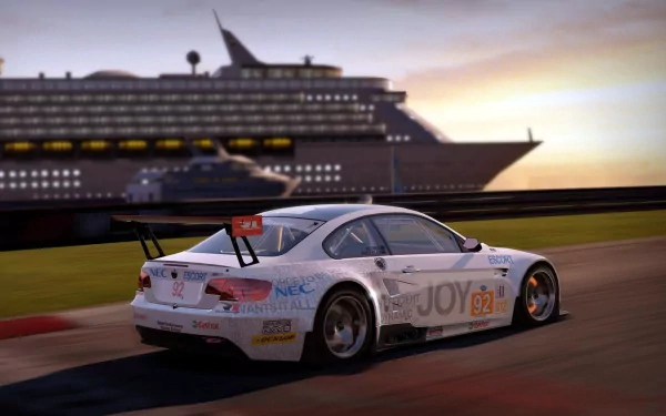 Need for Speed: Shift video game HD PC desktop wallpaper — white touring race car rounds a coastal track at sunset with a large cruise ship in the background.