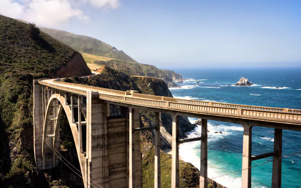 HD wallpaper of a scenic bridge spanning a rugged coastline with clear blue seas, set against green hills under a bright sky.