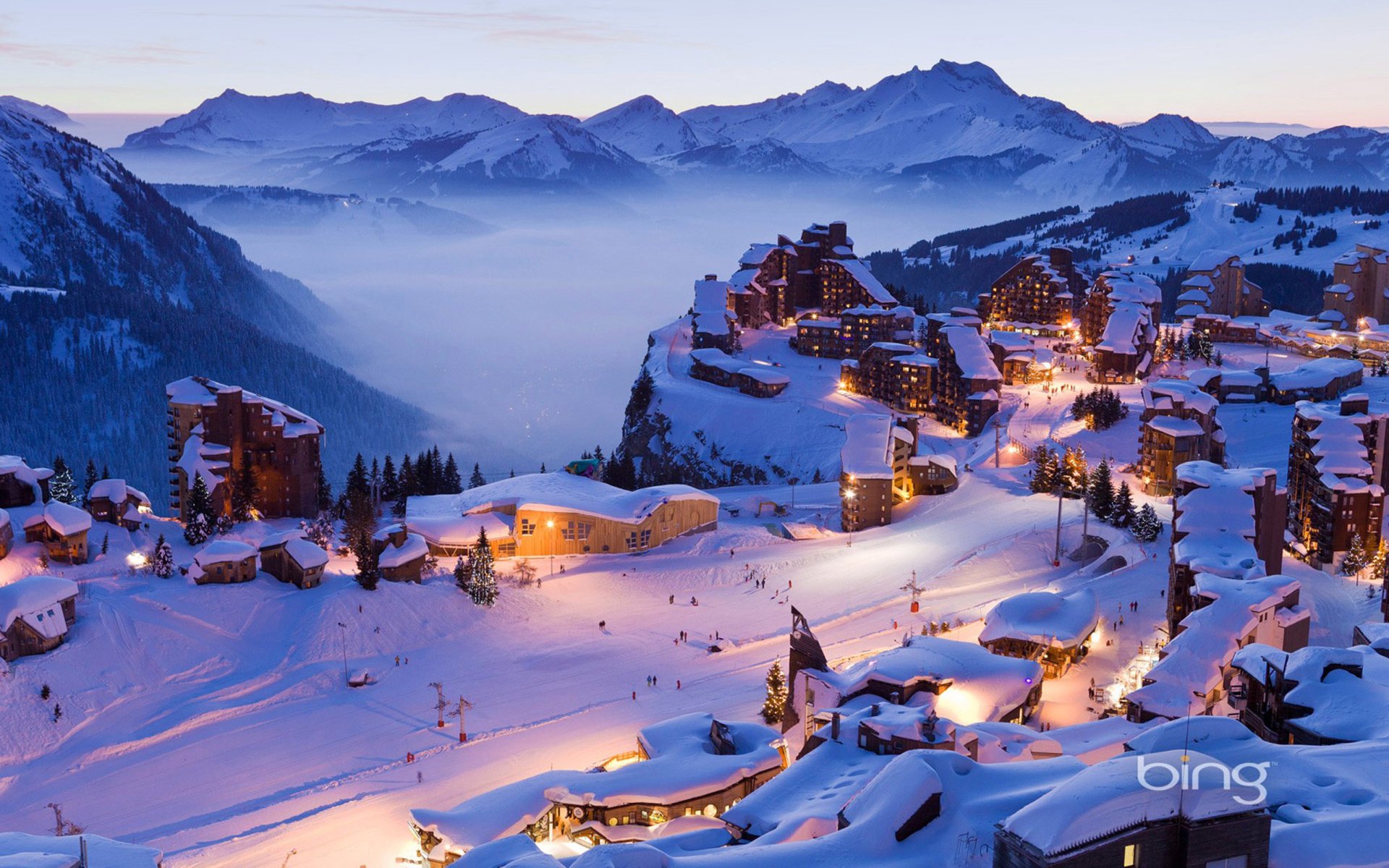 A picturesque winter village nestled in the mountains, featuring charming houses blanketed in snow, illuminated by soft lights against a serene, misty landscape.