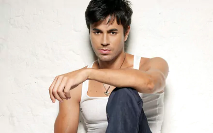 HD desktop wallpaper featuring Enrique Iglesias in a casual pose against a white background, wearing a white tank top and blue jeans. Tags include music and Enrique Iglesias.