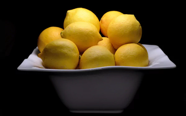 HD desktop wallpaper featuring a white bowl filled with bright yellow lemons against a black background, highlighting fresh food in vivid detail.