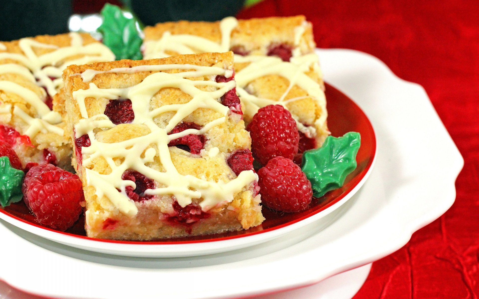 HD PC desktop wallpaper featuring close-up of raspberry pie bars decorated with white icing and fresh raspberries on a red and white plate.