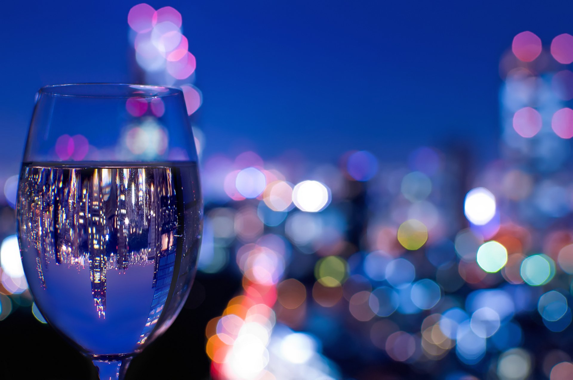 HD desktop wallpaper featuring a wine glass reflecting city lights against a vibrant bokeh background, blending food and wine themes with urban nightlife ambiance.