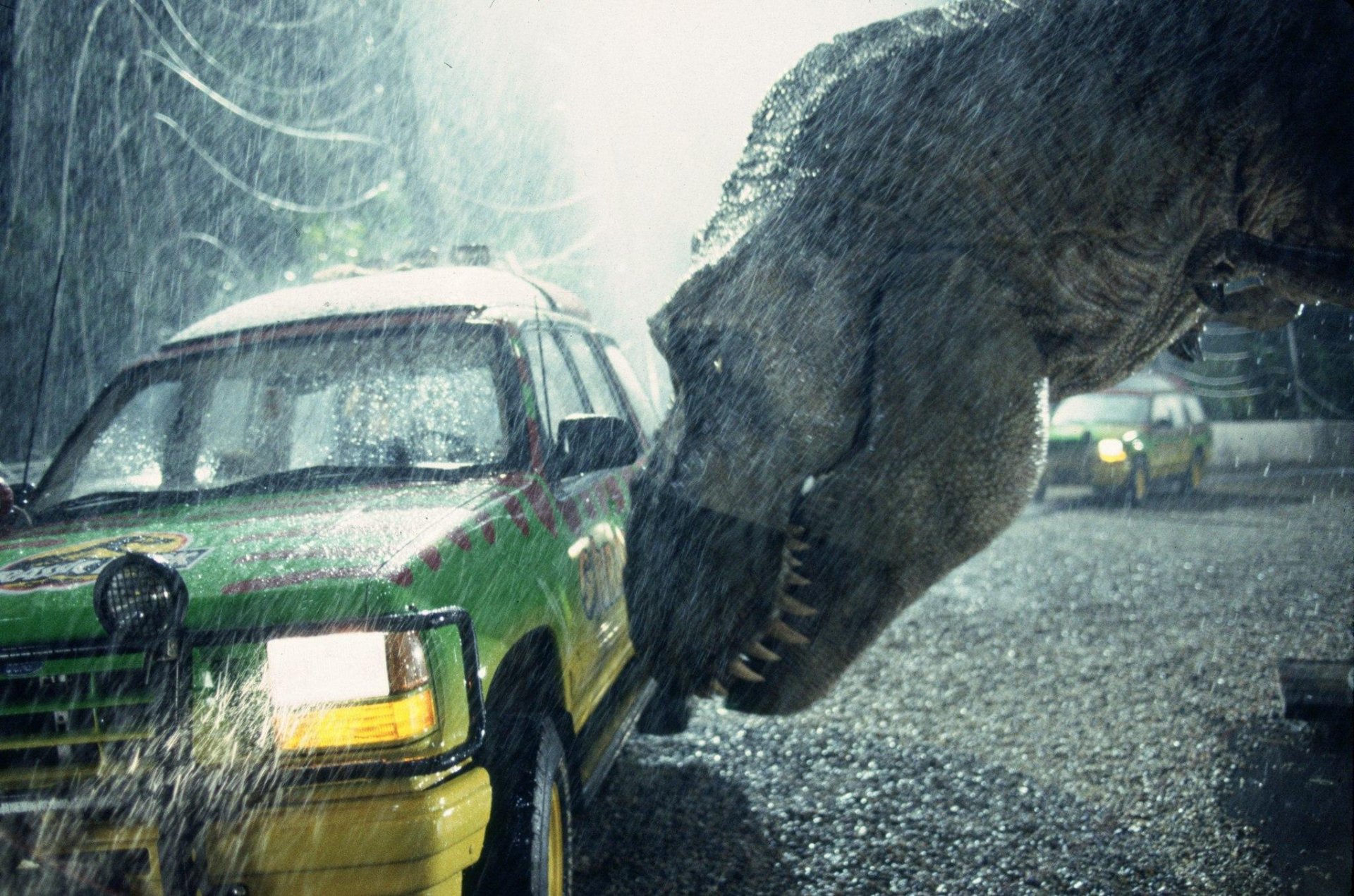 HD wallpaper of a Jurassic Park scene with a dinosaur approaching a vehicle in the rain.