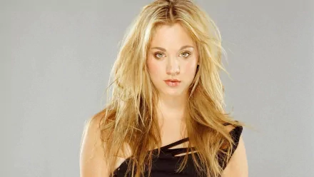 A striking HD desktop wallpaper featuring celebrity Kaley Cuoco with long, tousled blonde hair, exuding confidence against a neutral background.