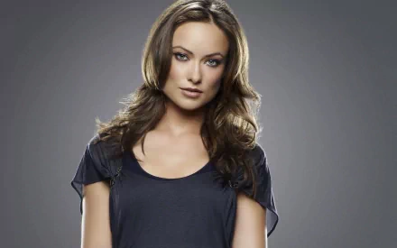 A high-definition desktop wallpaper featuring Olivia Wilde, exuding confidence with her striking gaze and elegant pose against a simple, muted background.