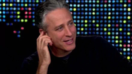 HD desktop wallpaper of a man from The Daily Show with Jon Stewart against a colorful lit background.