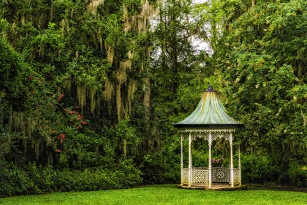 HD desktop wallpaper featuring a tranquil garden scene with a quaint gazebo surrounded by lush green bushes and draped trees.