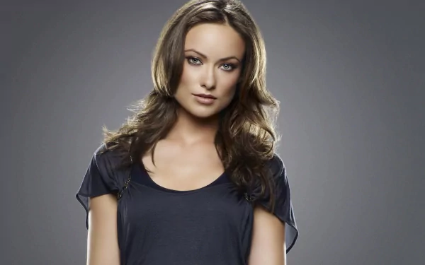 A high-definition desktop wallpaper featuring Olivia Wilde, exuding confidence with her striking gaze and elegant pose against a simple, muted background.