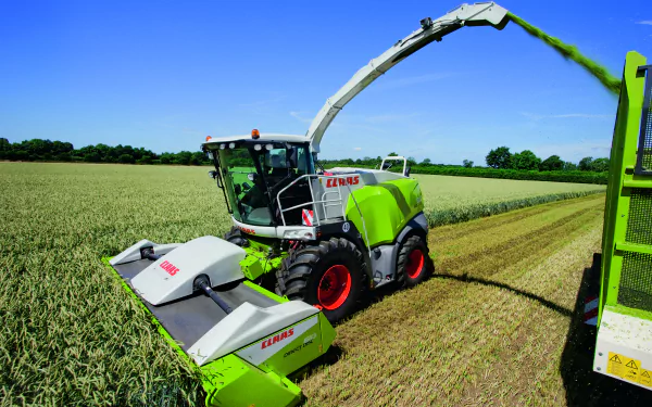 A Claas vehicle operates in a lush green field, harvesting crops under a clear blue sky. This stunning image serves as a vibrant 4K Ultra HD desktop wallpaper.