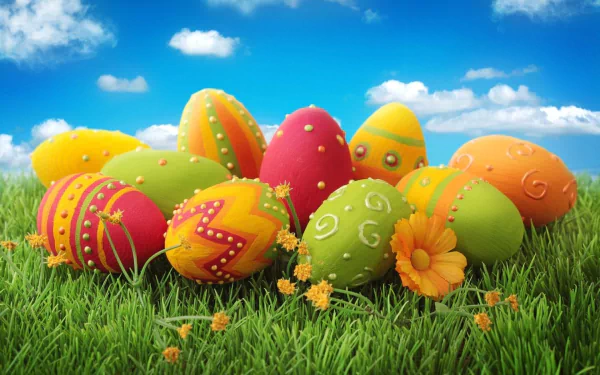 A vibrant collection of decorated Easter eggs rests on lush green grass, set against a bright blue sky with clouds, creating a joyful holiday atmosphere in this HD wallpaper.