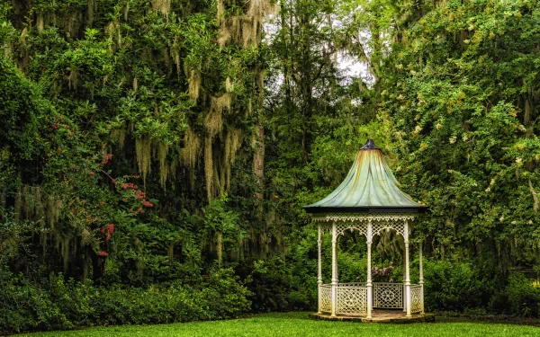 HD desktop wallpaper featuring a tranquil garden scene with a quaint gazebo surrounded by lush green bushes and draped trees.