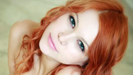 A close-up of a woman with vibrant red hair and striking green eyes, captured in a soft-focus background, making it a captivating HD desktop wallpaper and background.