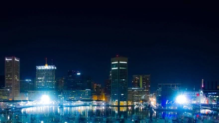 Nighttime Baltimore harbor skyline with illuminated man-made waterfront buildings reflected in water — HD PC desktop wallpaper.