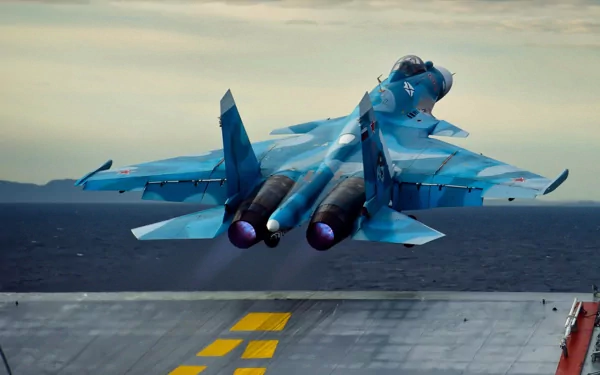HD PC desktop wallpaper and background: military Sukhoi Su-33 launching from an aircraft carrier, rear view with twin afterburners glowing over the ocean.