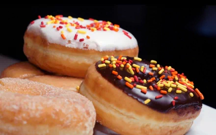 HD desktop wallpaper featuring close-up of assorted doughnuts with colorful sprinkles and glaze on a dark background.