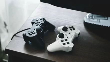 A high-definition desktop wallpaper featuring a black and white Sony PlayStation controllers resting on a wooden surface, showcasing a sleek gaming aesthetic.