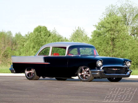 HD PC desktop wallpaper of a classic two-tone Chevrolet coupe with chrome wheels parked on pavement before green trees.