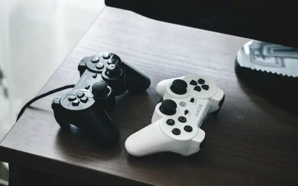 A high-definition desktop wallpaper featuring a black and white Sony PlayStation controllers resting on a wooden surface, showcasing a sleek gaming aesthetic.