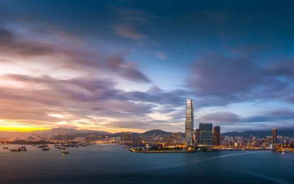 HD desktop wallpaper showing the iconic Hong Kong skyline at sunset with illuminated skyscrapers and calm harbor waters under a dramatic sky.